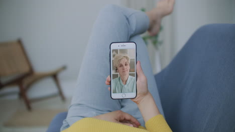Over-shoulder-view-of-young-woman-daughter-video-calling-old-parent-mother-or-mature-friend-using-conference-chat-online-application-on-mobile-phone-screen-at-home-office.-Family-videocall-concept